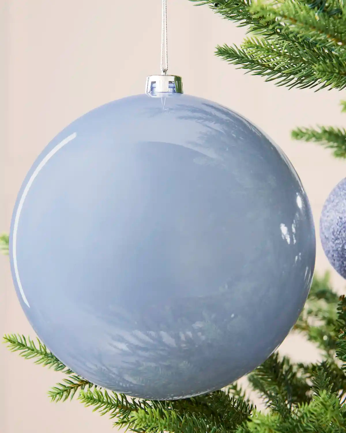 Close-up of an ice blue 20 cm oversized shatterproof bauble with a smooth shiny finish on a Christmas tree.
