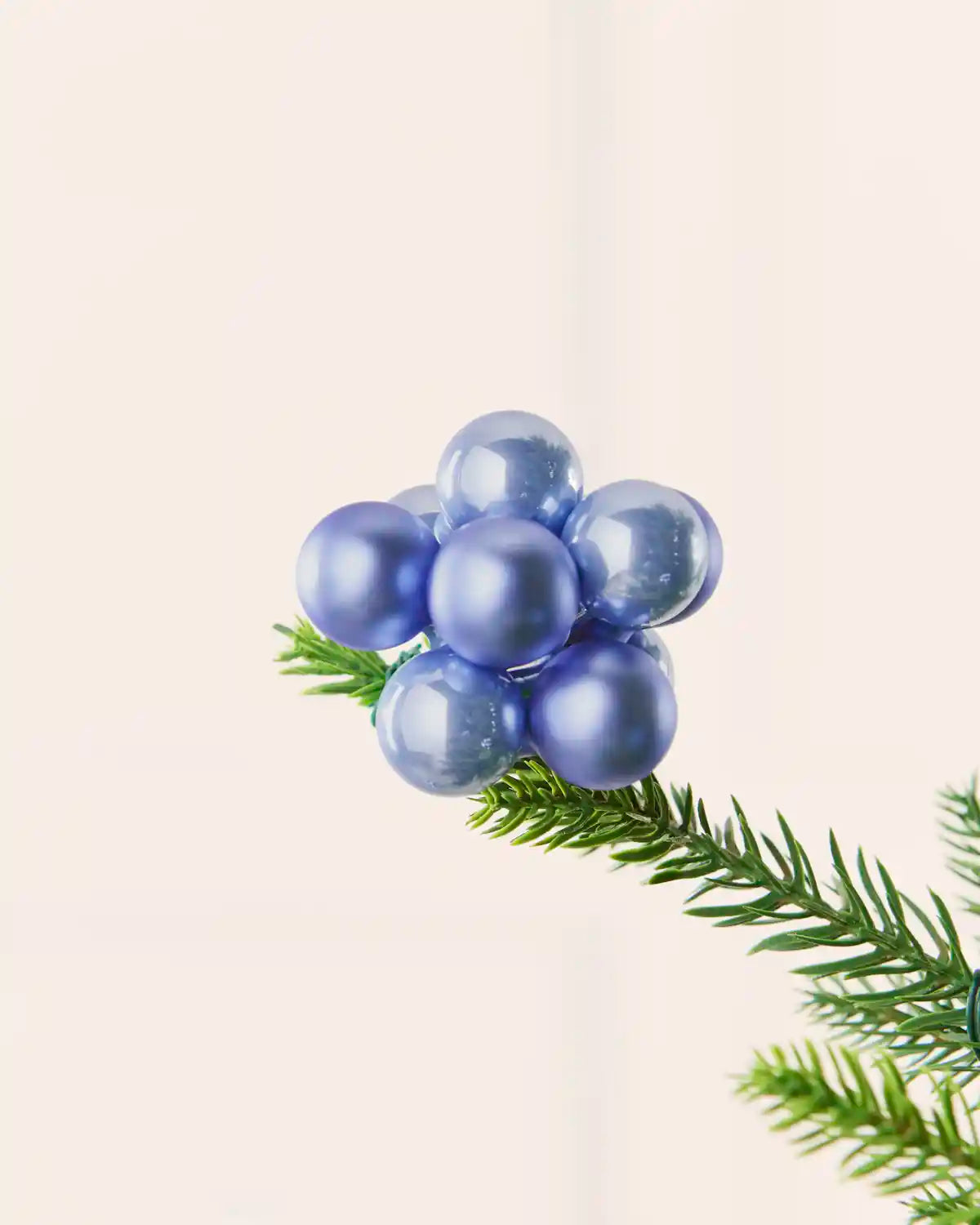 Close-up of an ice blue glass berry cluster bauble attached to a Christmas tree branch.
