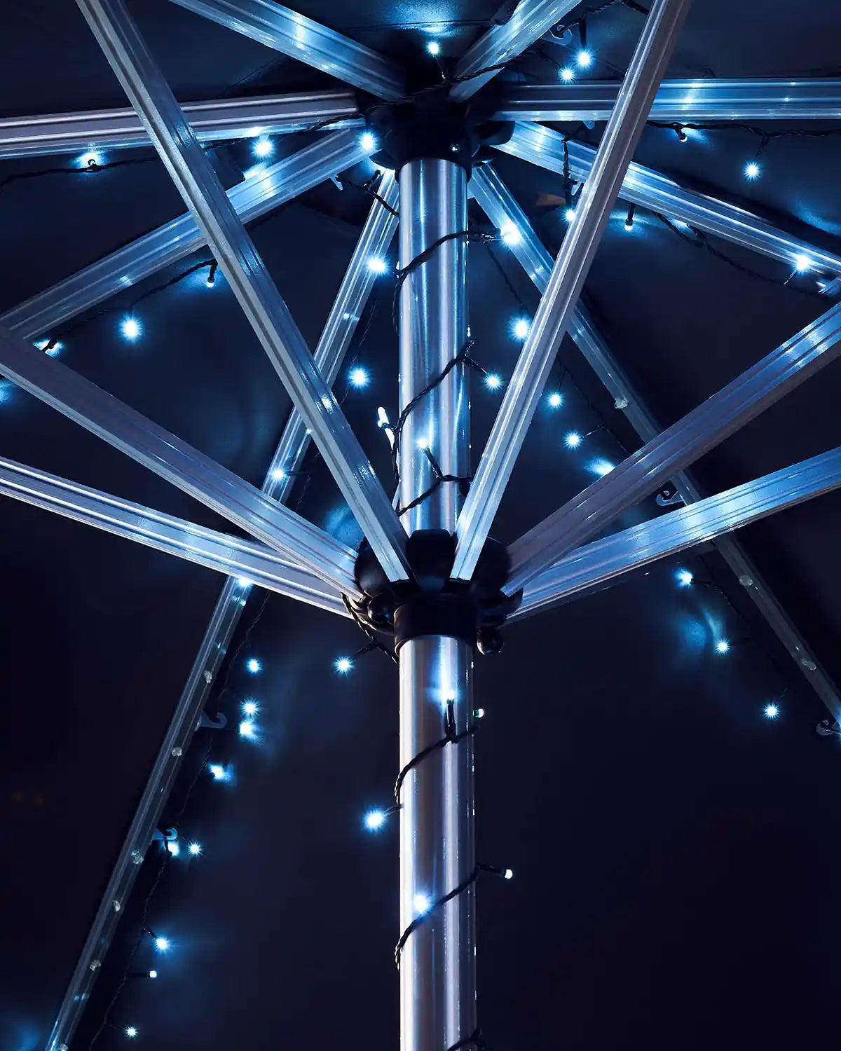 Close-up of an umbrella pole with ice white fairy lights against a dark background