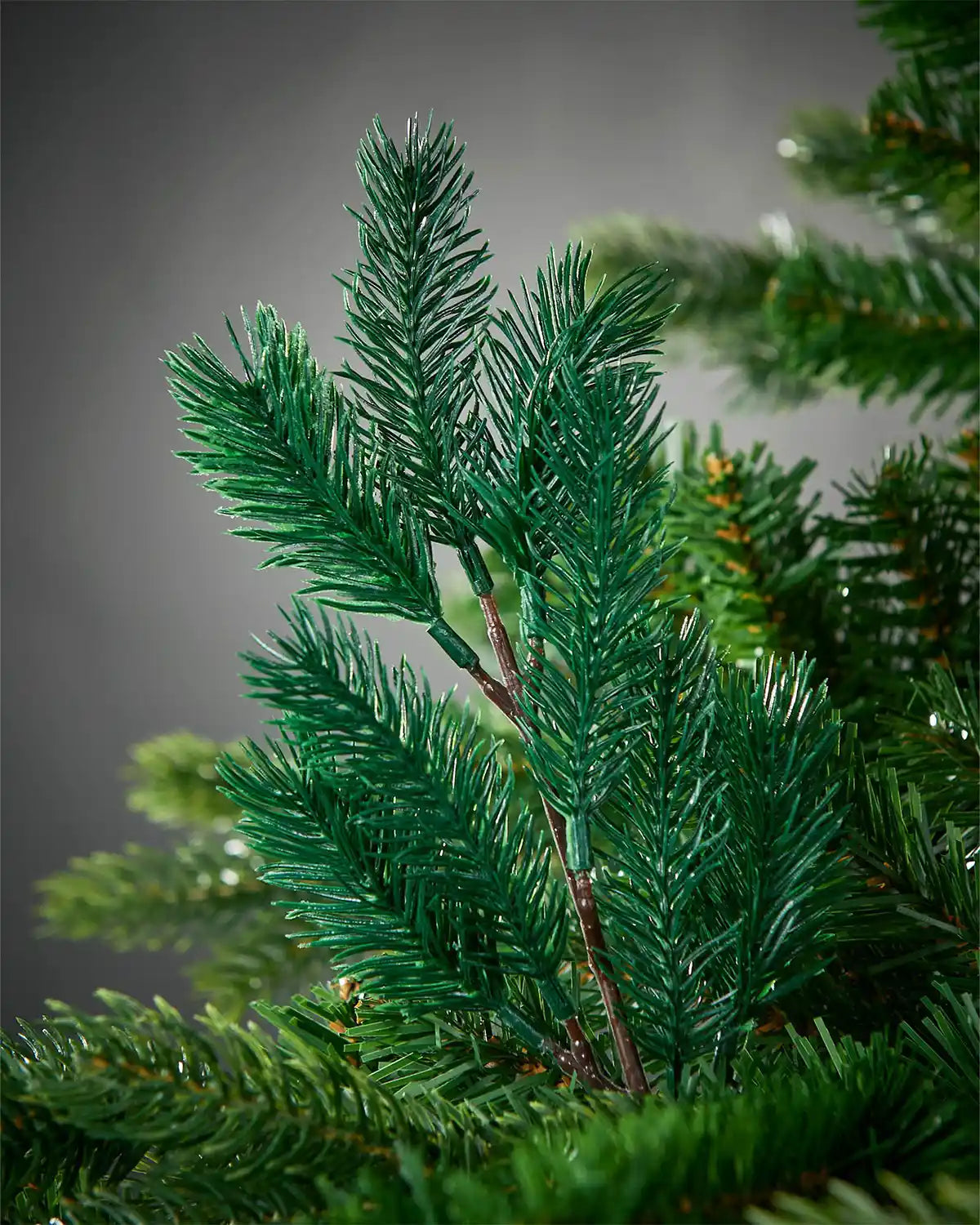 Close-up of artificial greenery pick on a Christmas tree against a grey background