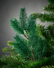 Close-up of artificial greenery pick on a Christmas tree against a grey background