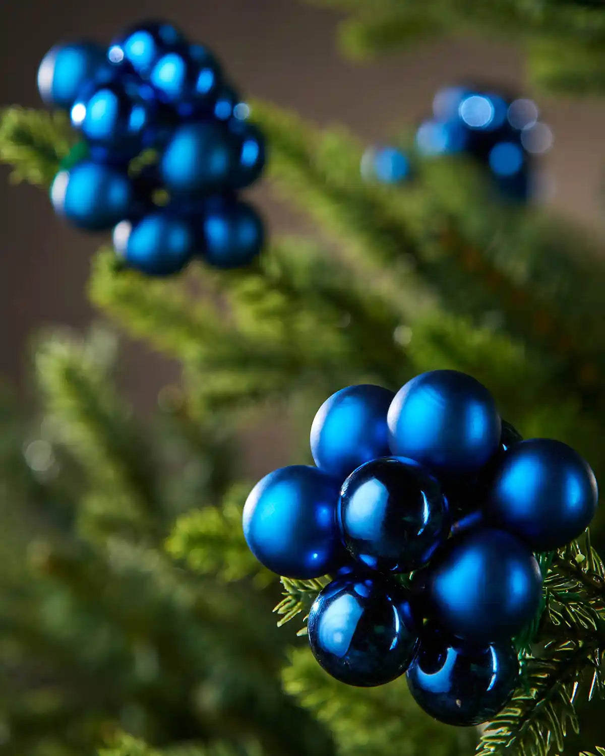 Close-up of blue berry decorations on a green branch against a blurred background