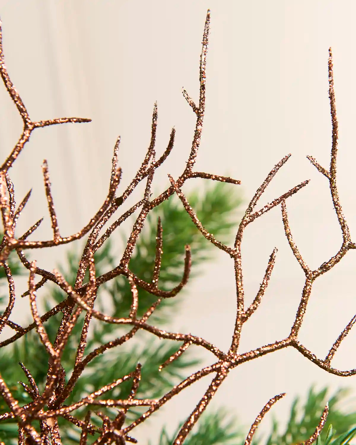Close-up of glittery espresso brown decorative branches or antler-like ornaments against a soft off-white background with blurred green foliage.