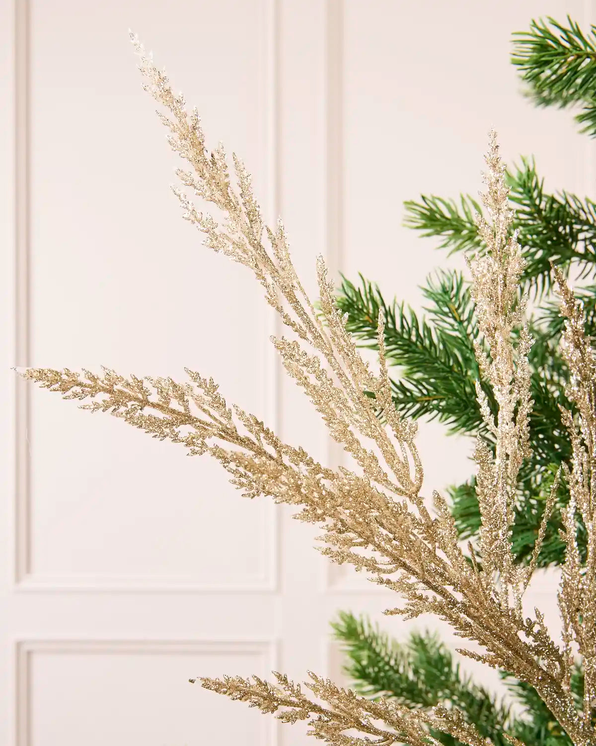 Close-up of gold glitter decorative branches with green Christmas tree branches against a cream paneled background