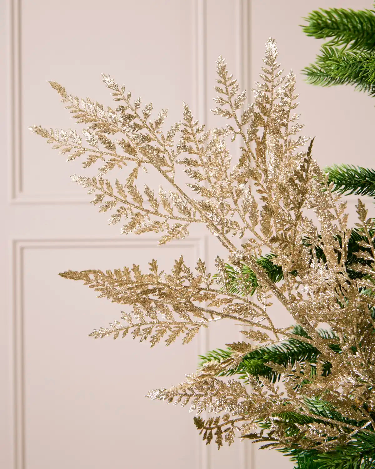 Close-up of gold glitter leaves on branching stems displayed among Christmas tree branches