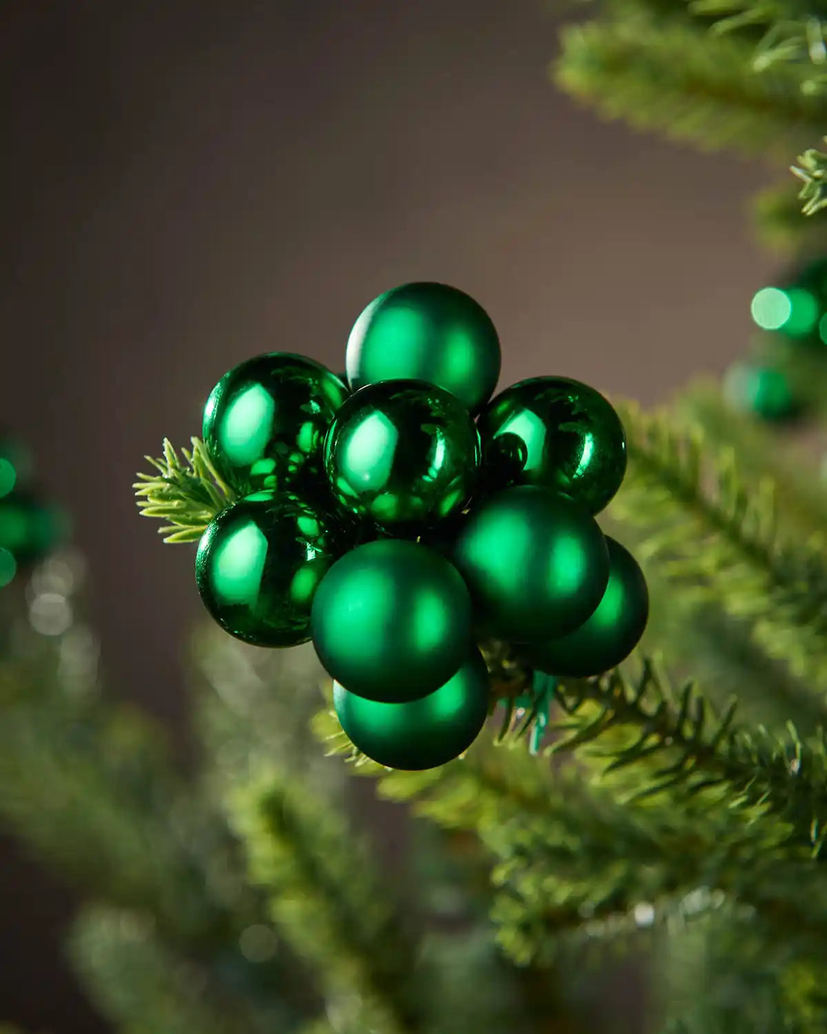 Close-up of green Christmas ornaments on a tree branch with a blurred background