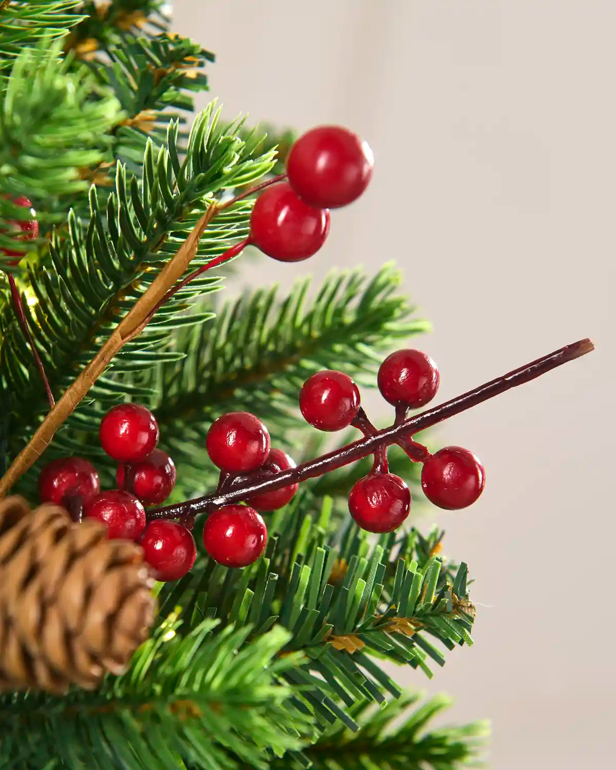 Close-up of green evergreen branches featuring clusters of glossy red berries and a pinecone