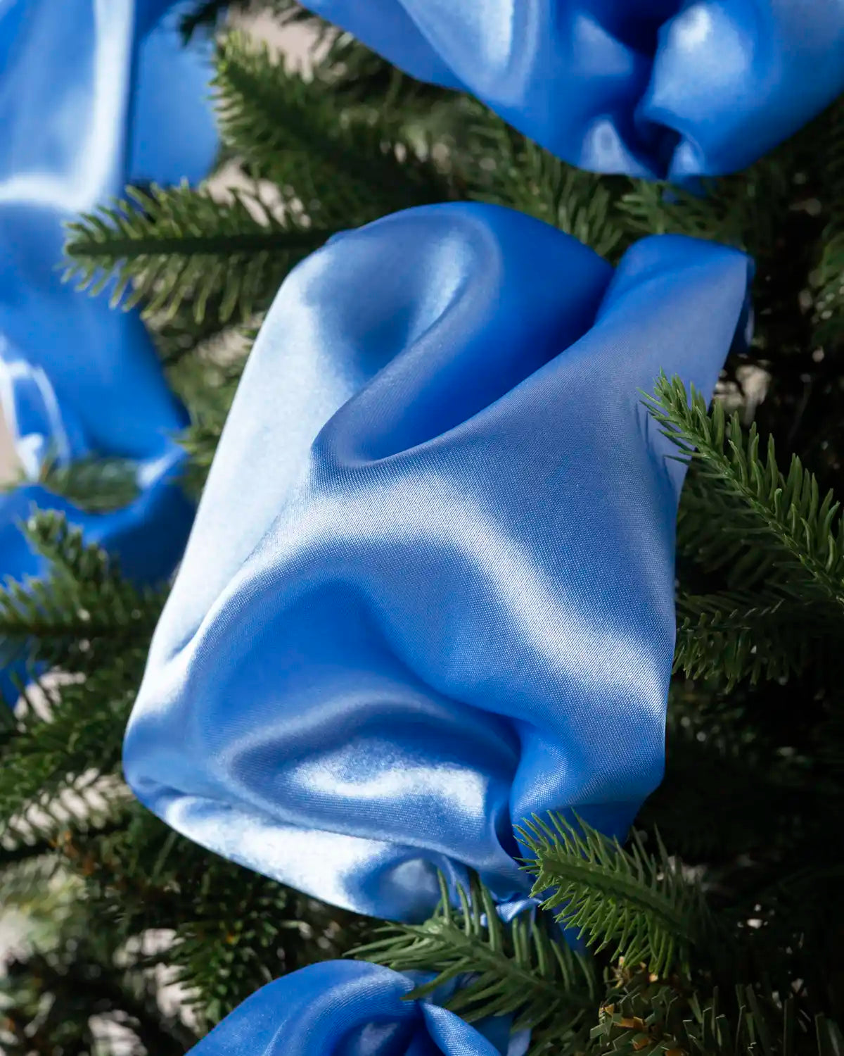 Close-up of ice blue satin ribbon wrapped around the branches of a Christmas tree