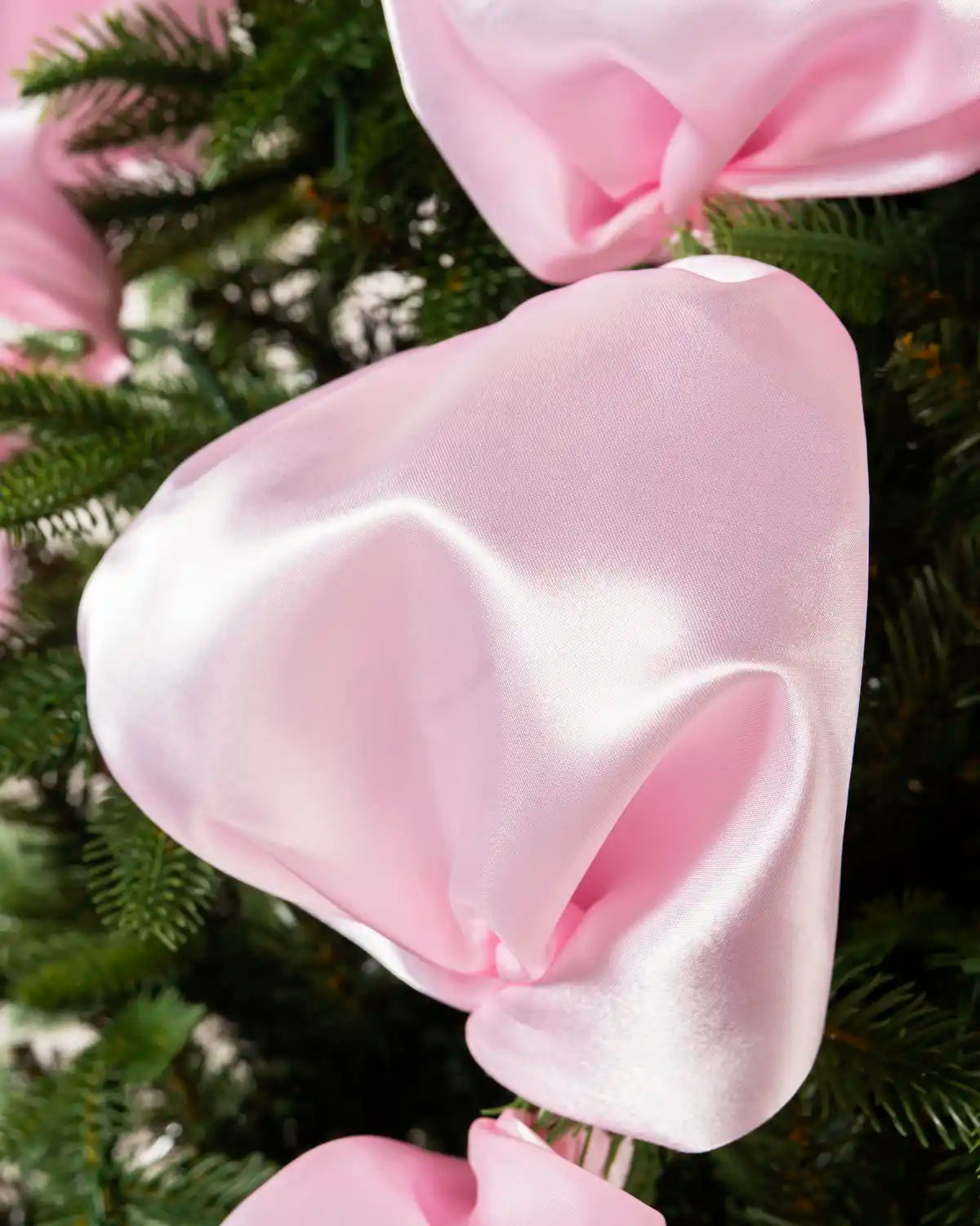 Close-up of pink satin ribbon wrapped around the branches of a Christmas tree