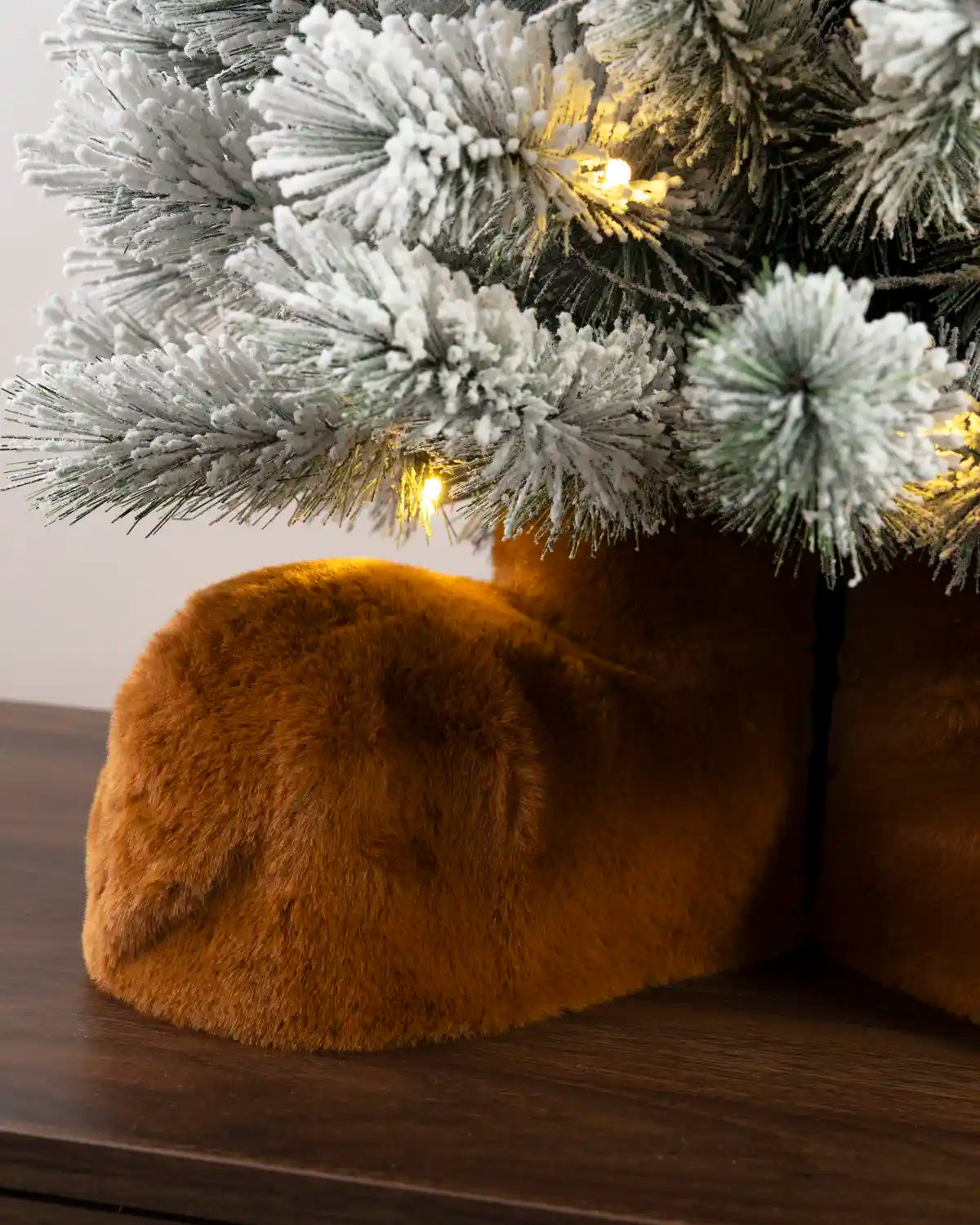 Close-up of plush brown reindeer feet beneath a flocked Christmas tree