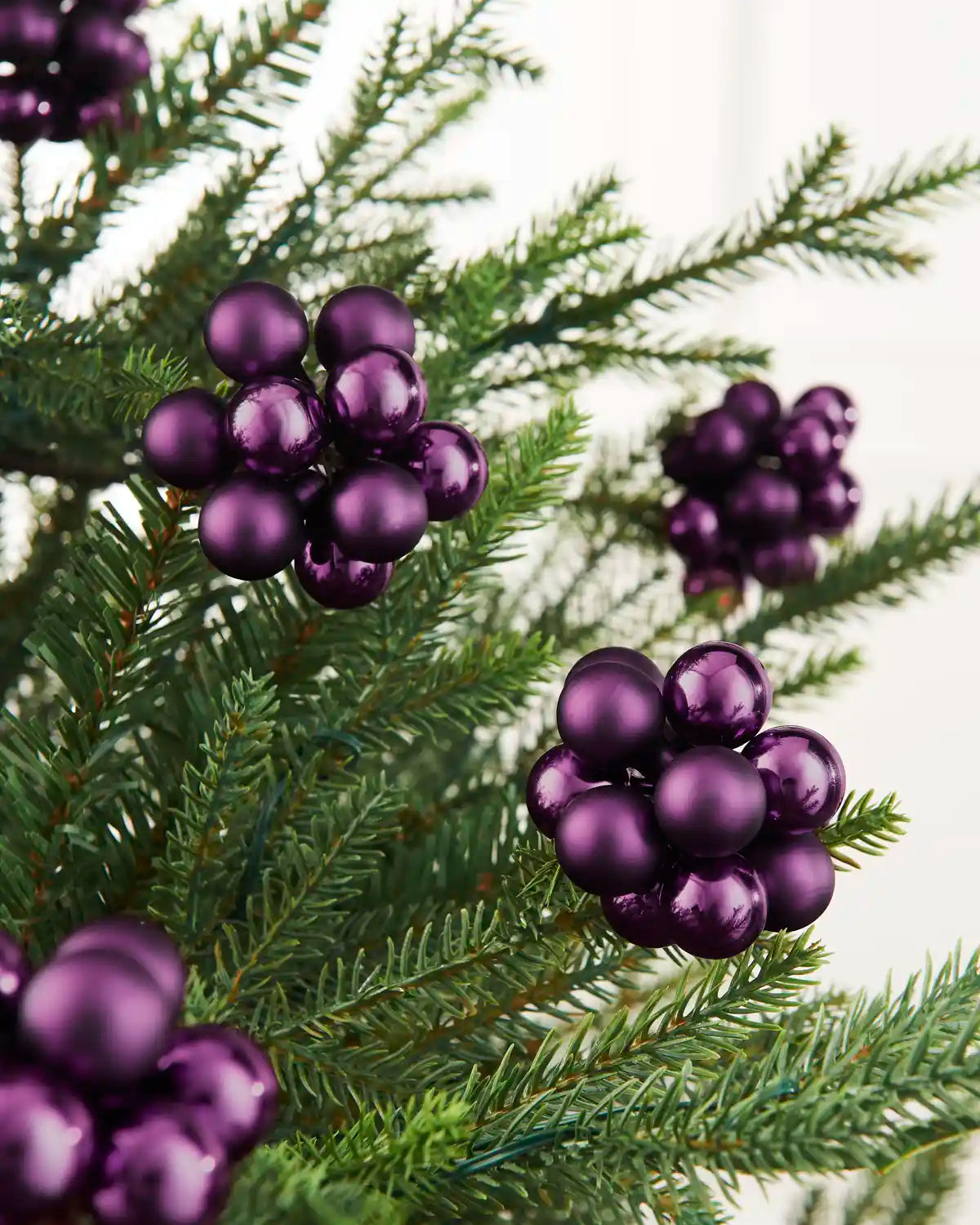 Close-up of purple glass berry cluster baubles with shiny and matt finishes on a Christmas tree.
