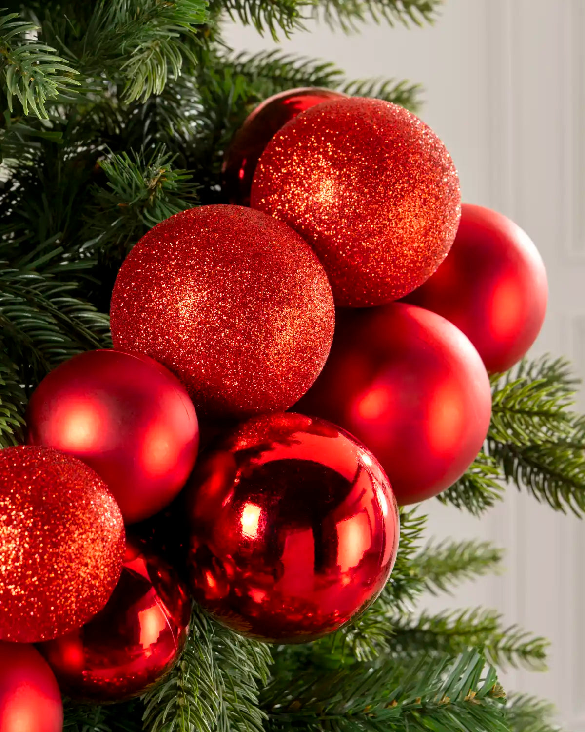 Close-up of red baubles in a Red Bauble Cluster Arch, featuring glitter, matte, and glossy finishes against green tree branches