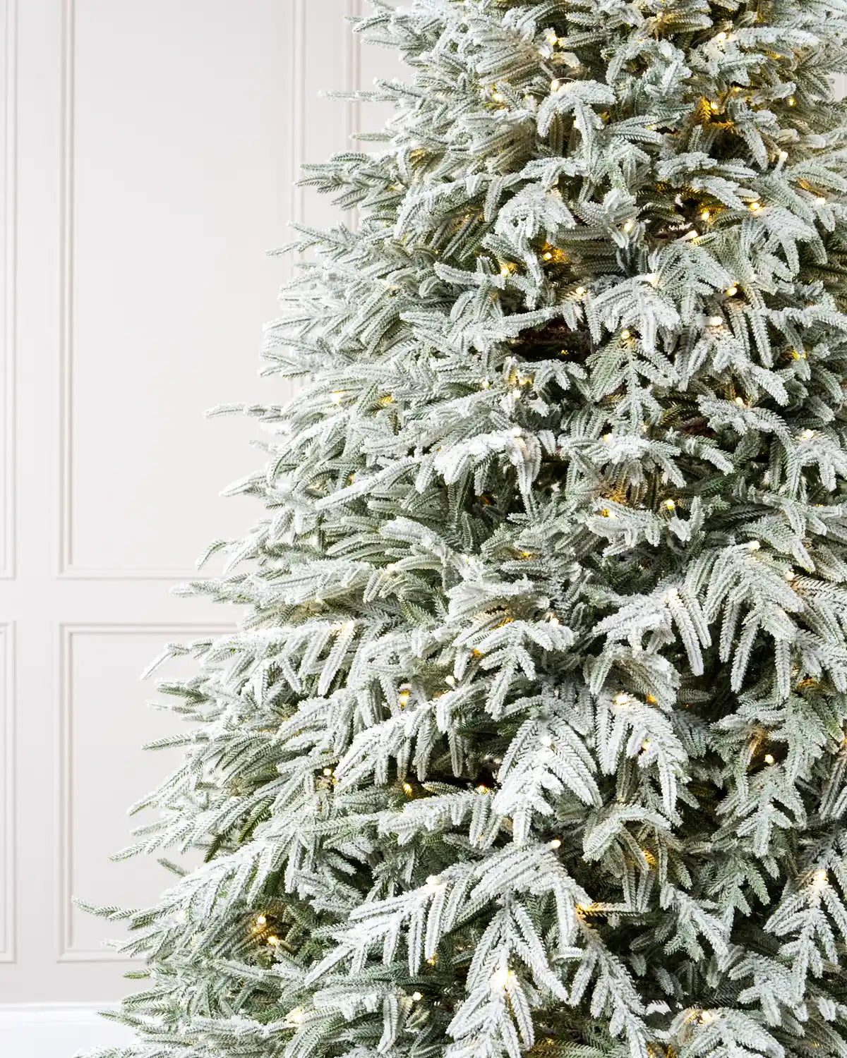 Close-up of snow-covered artificial Christmas tree branches with warm white lights, showcasing the frosted green needles