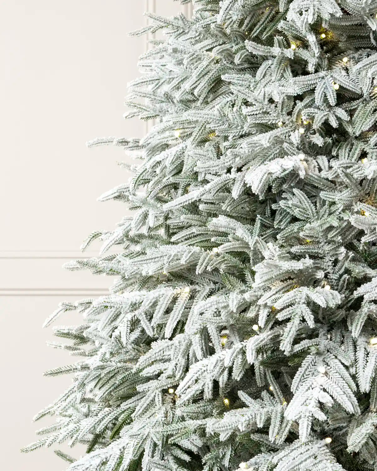 Close-up of snow-flocked branches on a pre-lit Grand Duchess Christmas tree, showing white-coated needles and warm white lights