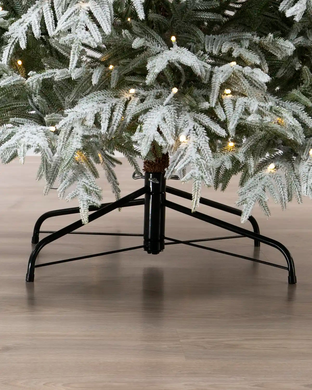 Close-up of the black metal stand supporting a pre-lit snow-flocked Grand Duchess Christmas tree