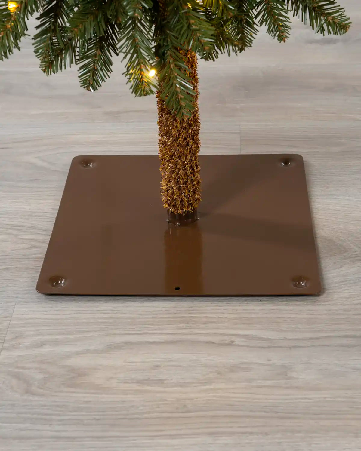 Close-up of the brown square base supporting the slim Christmas tree.