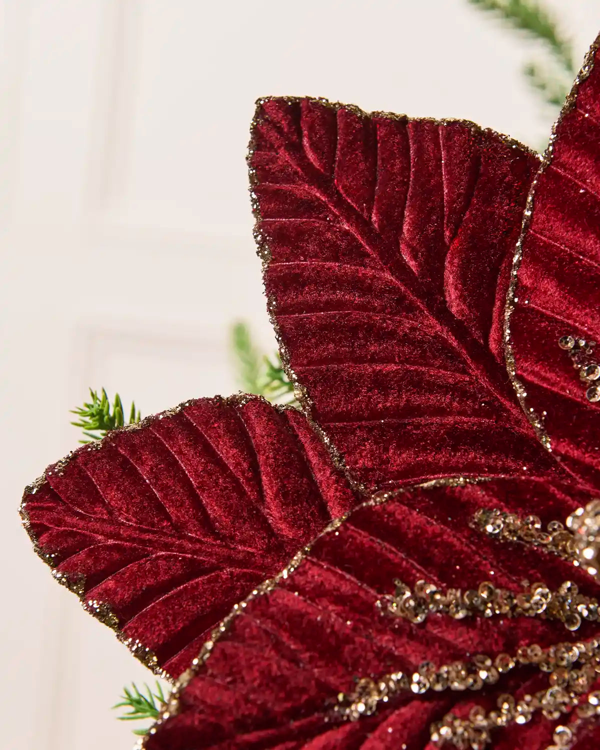 Close-up of the burgundy poinsettia’s velvet petals, highlighting the textured fabric, veining, and gold glitter trim