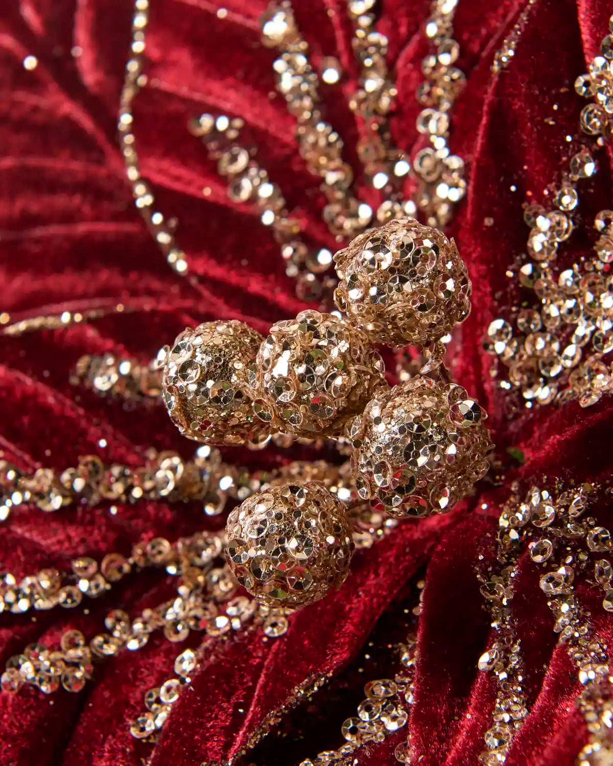 Close-up of the burgundy poinsettia showing gold glittered berry clusters and sequin embellishments on the petals