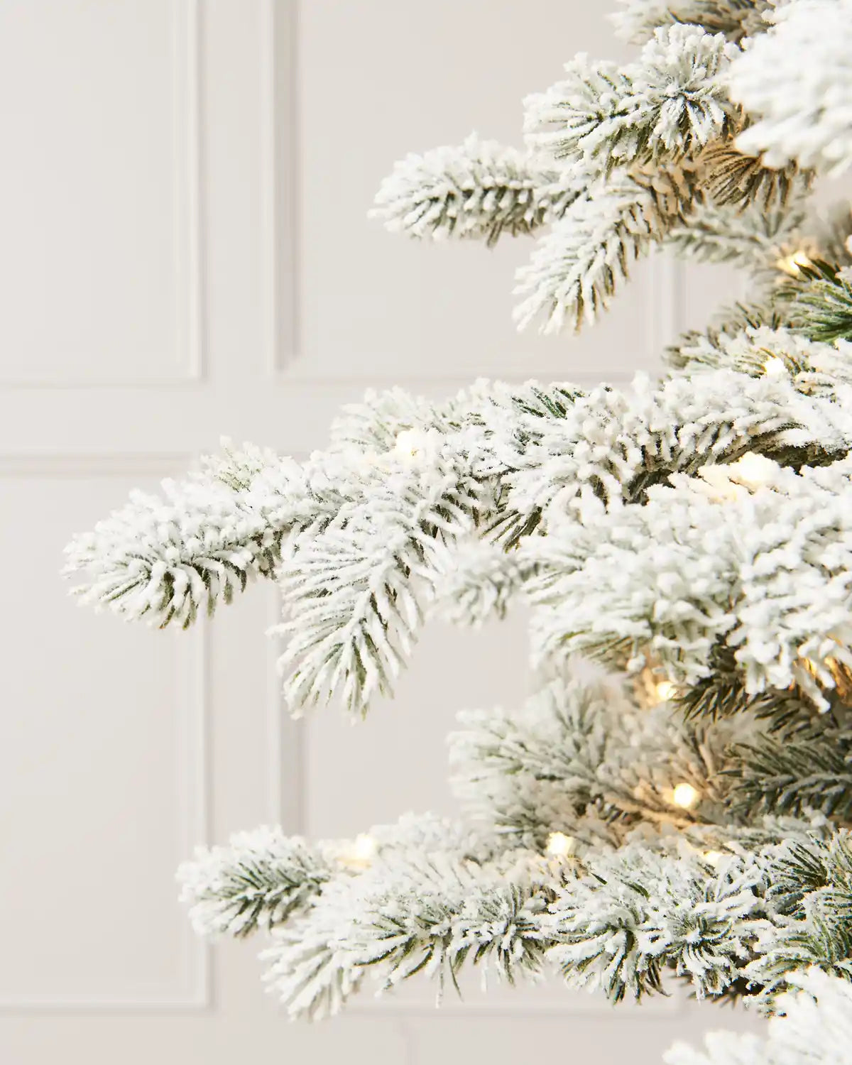 Close-up of the flocked Christmas tree’s branches, showing snow-covered needles, and softly glowing warm white lights.