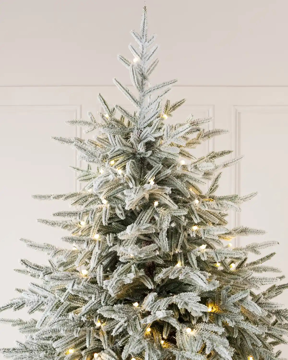 Close-up of the flocked Christmas tree’s top branches, showing the upright central leader, snow-covered needles