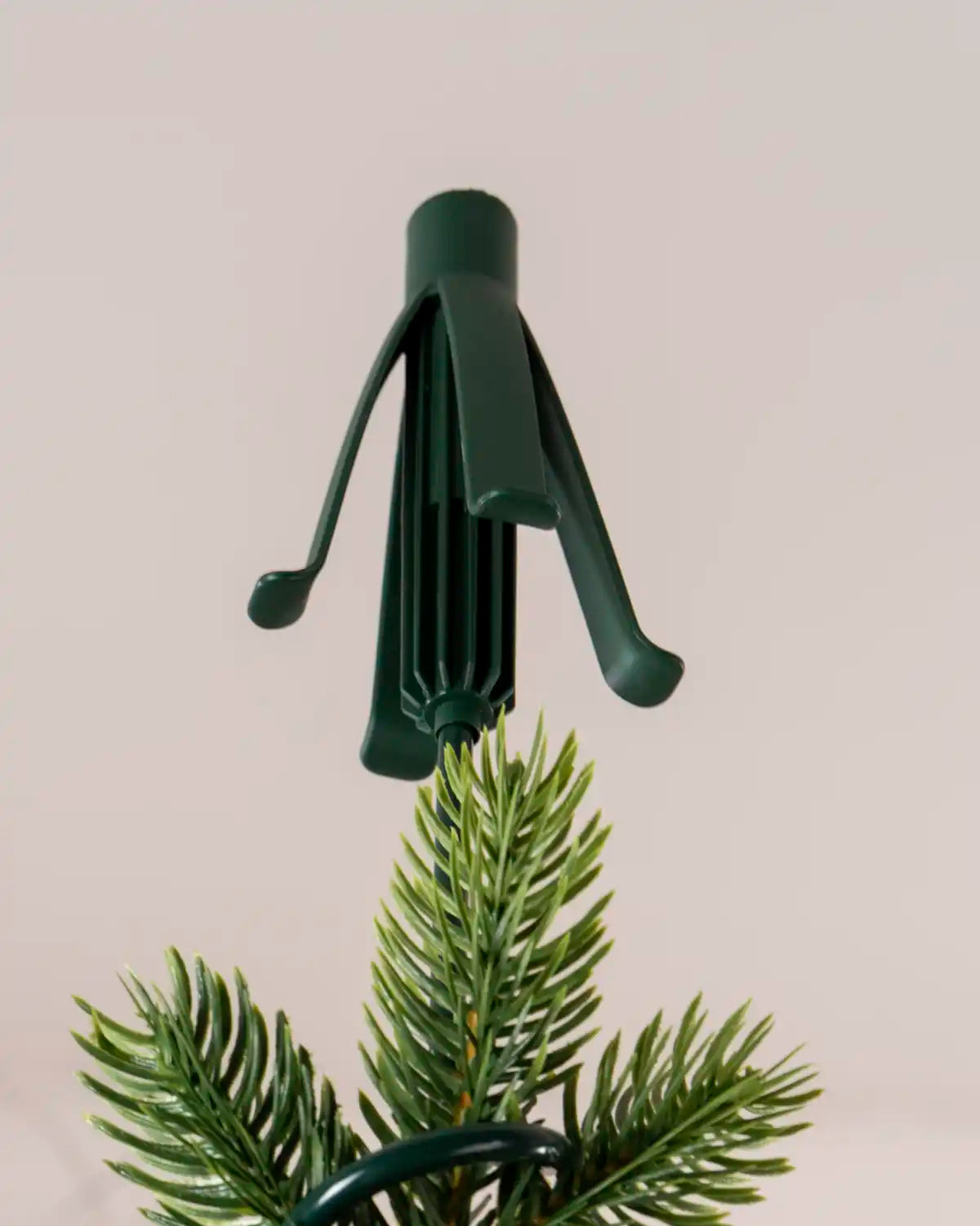 Close-up of the green Christmas tree topper holder fitted over the top of an artificial tree, with the holder’s support arms visible