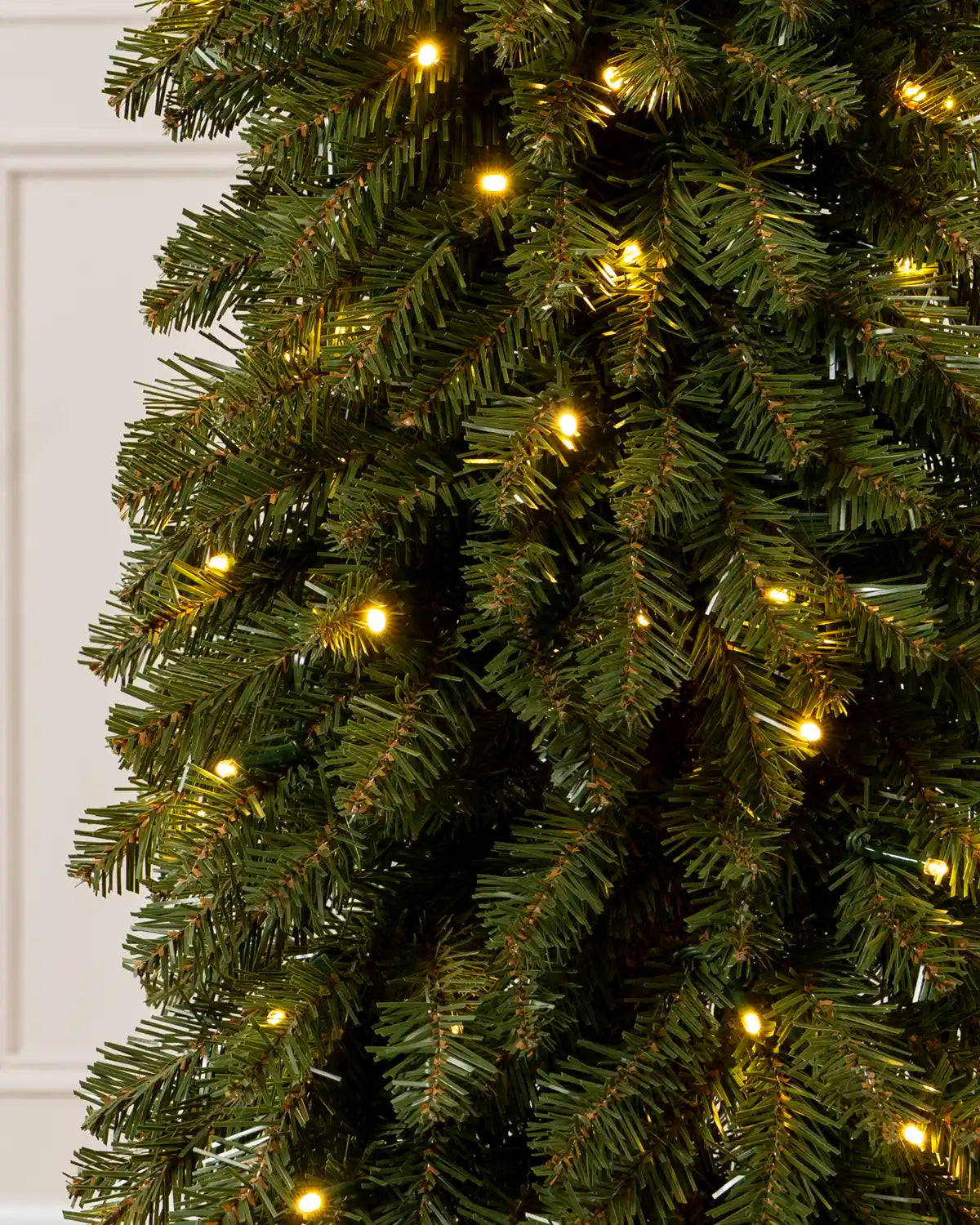 Close-up of the green branches and warm white lights on a slim Christmas tree.