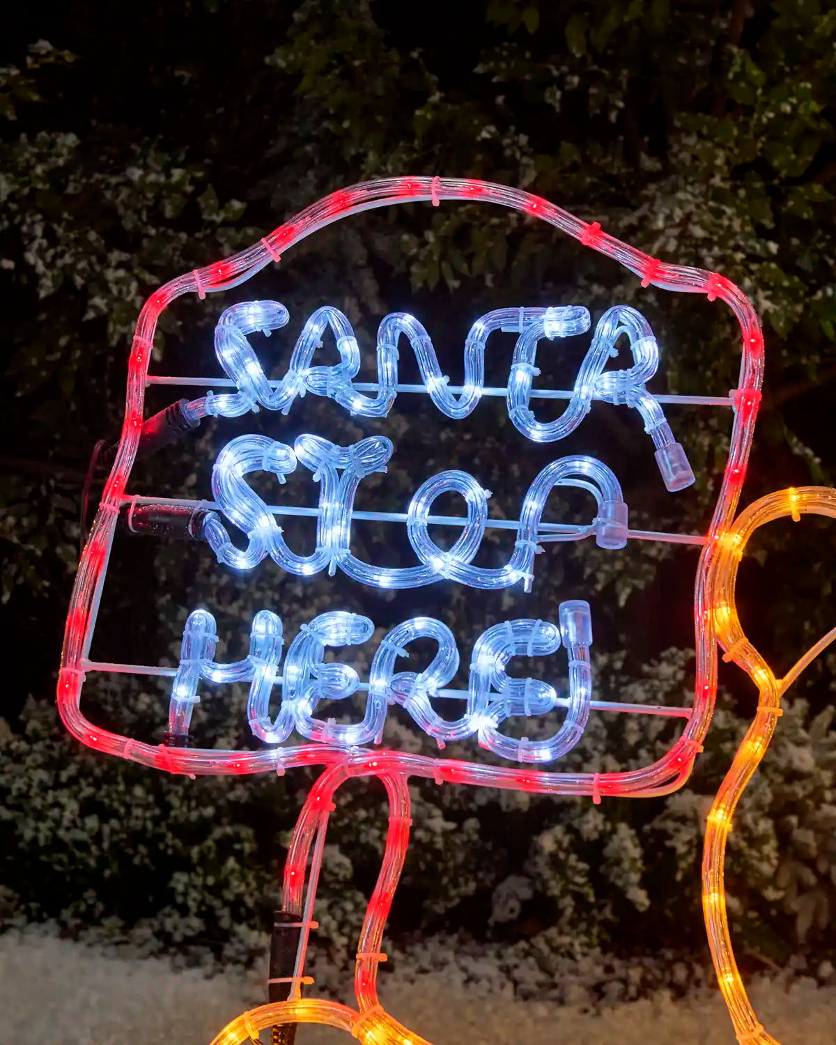 Close-up of the illuminated “Santa Stop Here” sign, outlined in red rope light with white glowing lettering