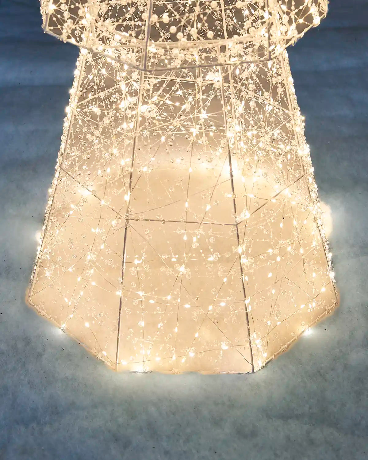 Close-up of the illuminated base of the Pre-Lit Twinkling Beaded Christmas Tree standing in snow with warm white lights