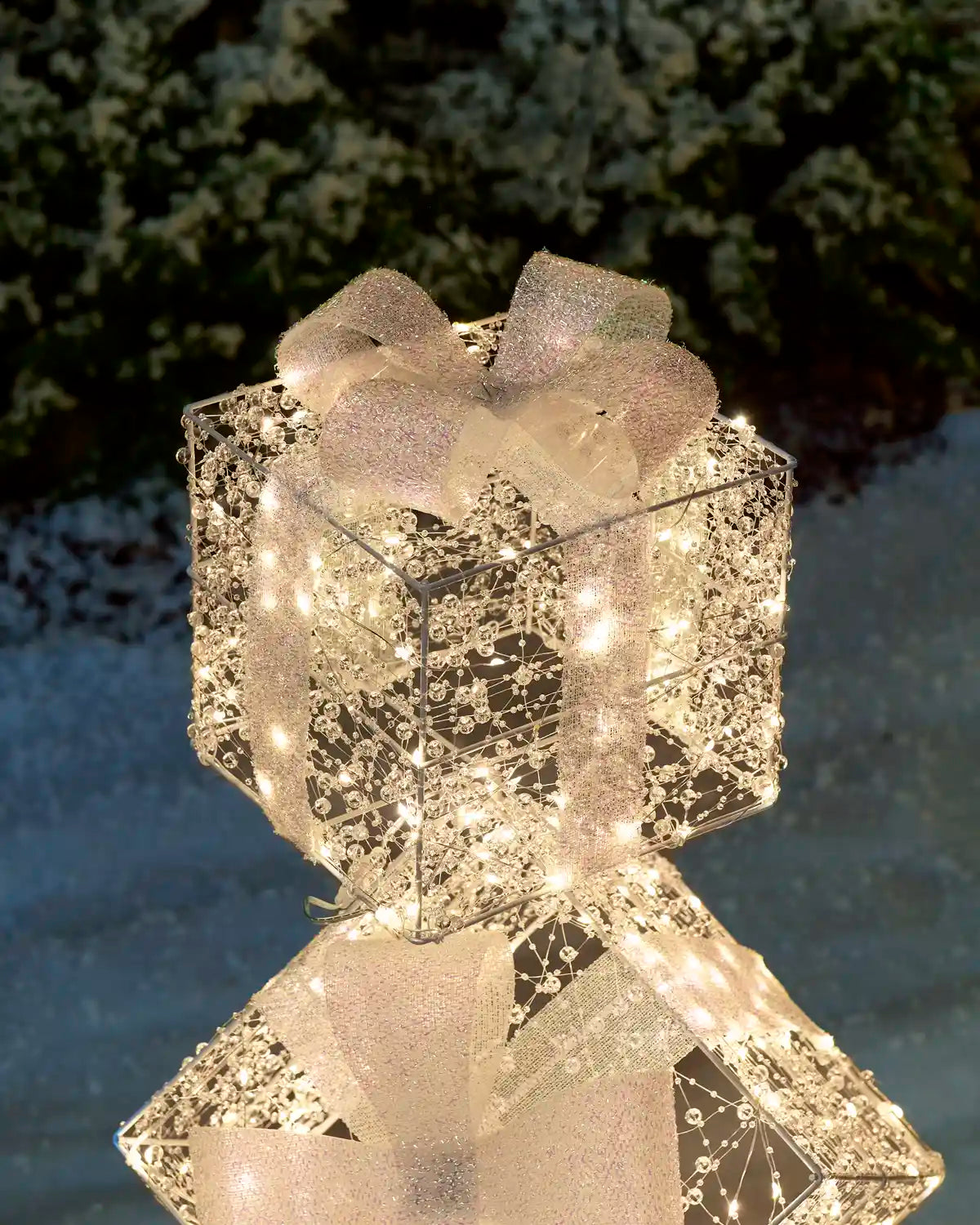 Close-up of the illuminated top present of the Pre-Lit Twinkling Present Stack standing in snow with warm white lights