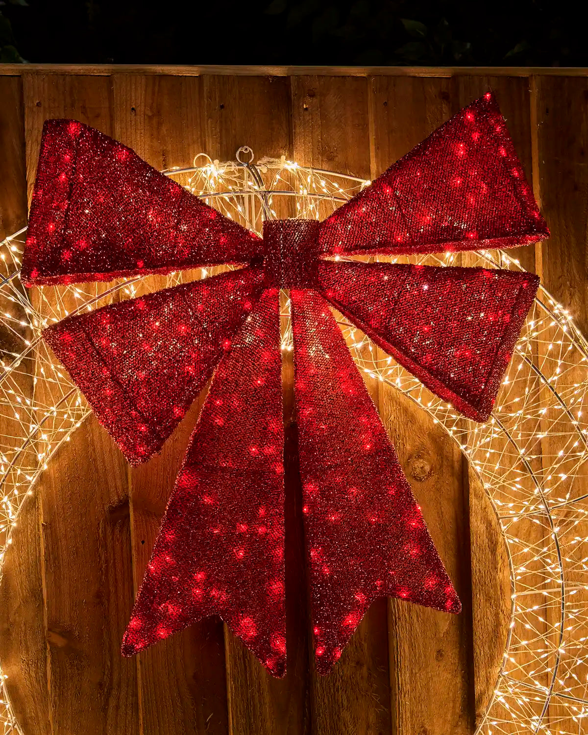 Close-up of the large red glitter bow centered on the Pre-Lit Twinkling Wreath Silhouette, with warm white lights visible around the wreath