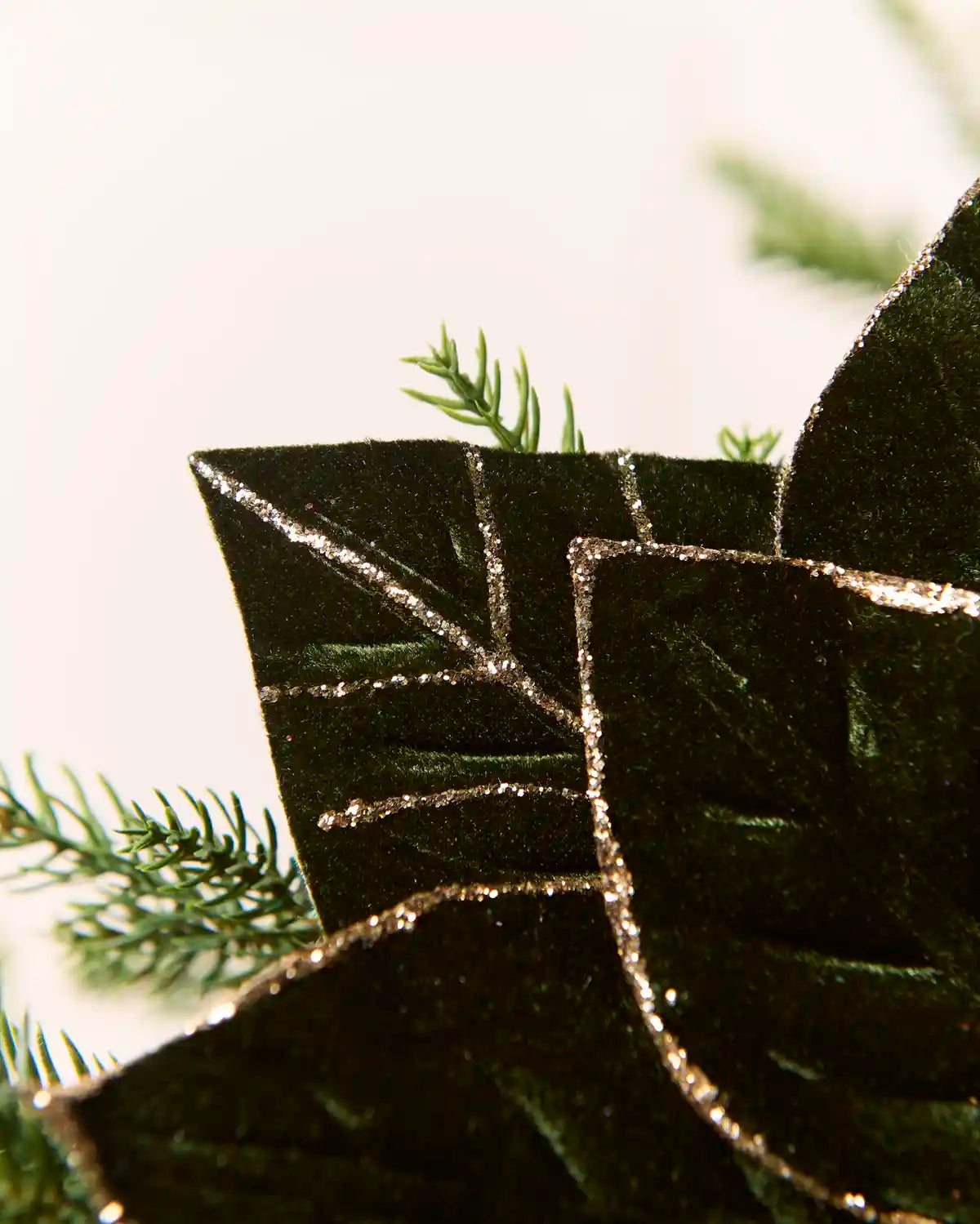 Close-up of the pointed sage green poinsettia petals showing the textured fabric and gold glitter outlining the edges and vein patterns.