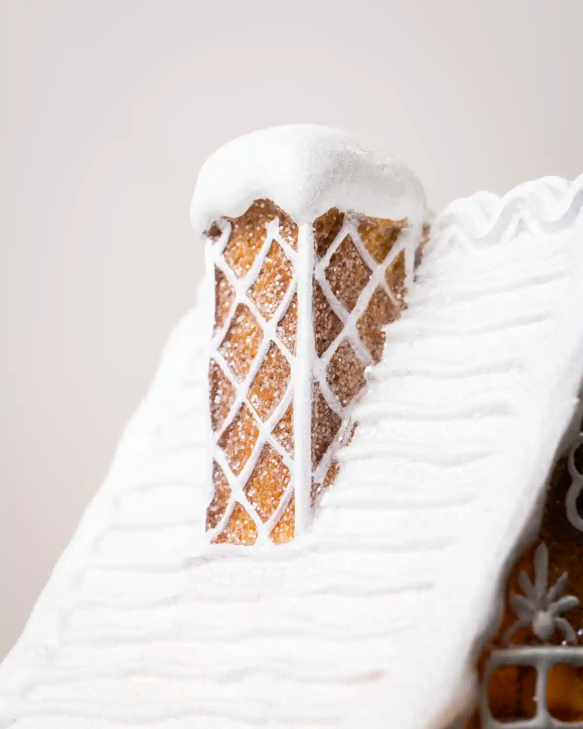 Close-up of the pre-lit gingerbread house roof, showing thick white snow-like icing and decorative crisscross icing details on the chimney