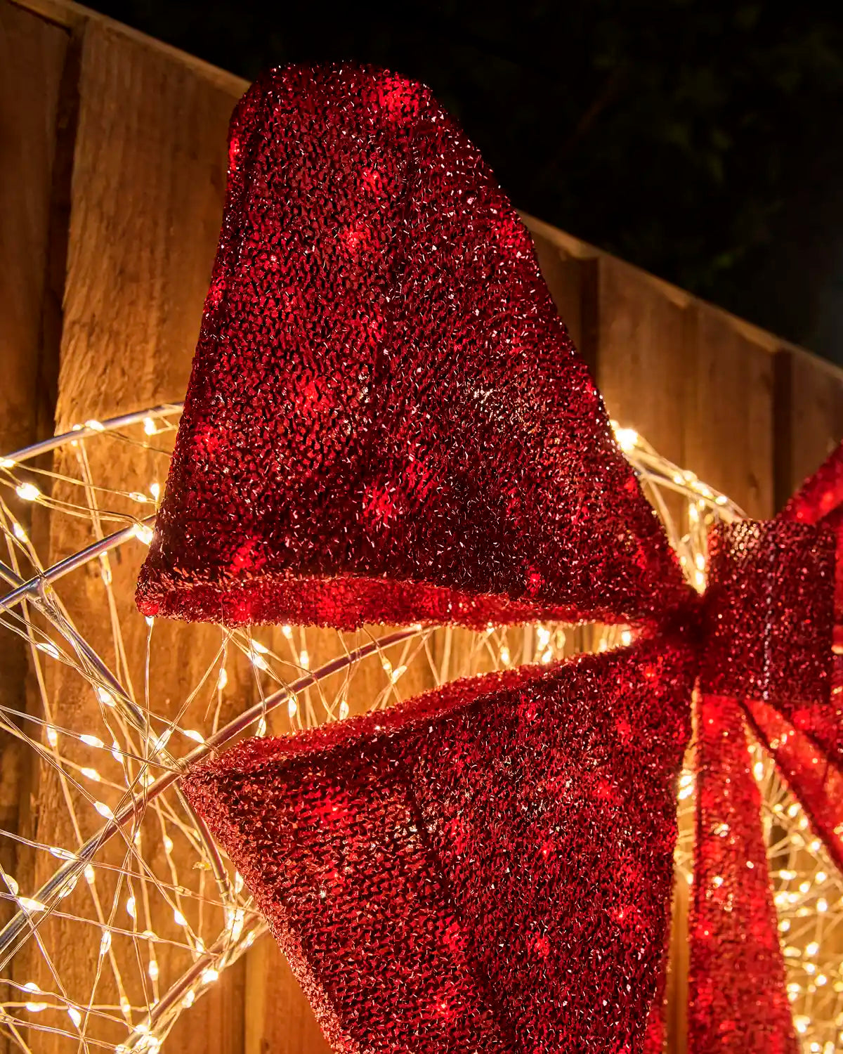 Close-up of the sparkling red glitter bow on the Pre-Lit Twinkling Wreath Silhouette, with warm white lights glowing behind it