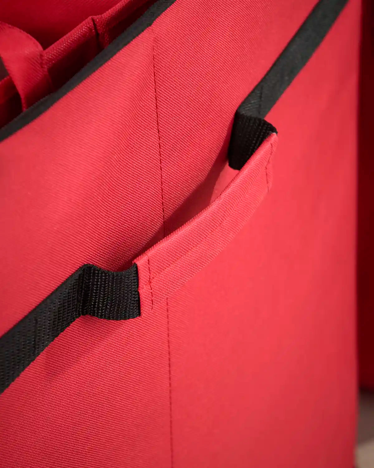 Close-up of the storage bag’s durable red fabric construction and black reinforced trim with secure fastening detail