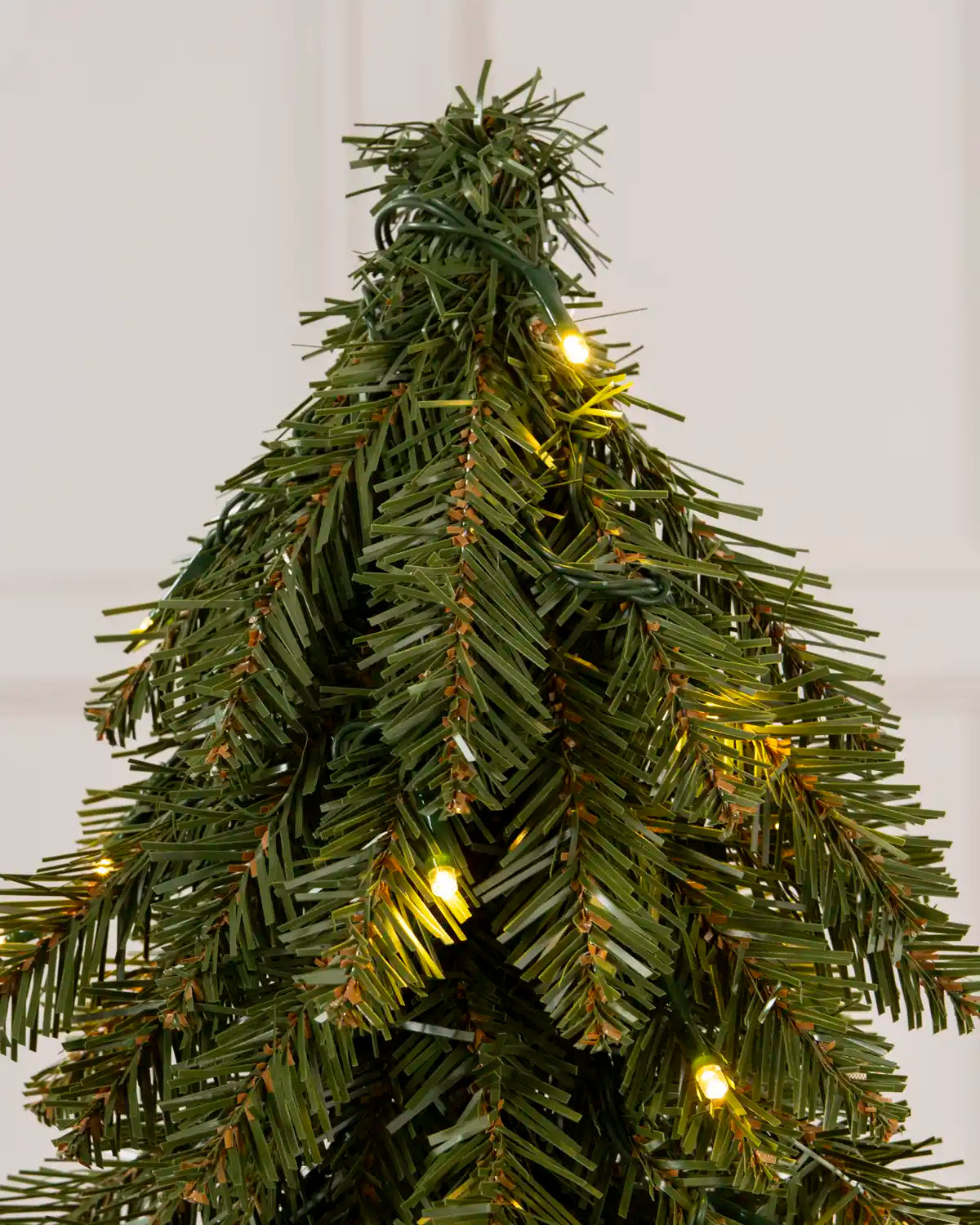 Close-up of the top section of a slim green Christmas tree with warm white lights