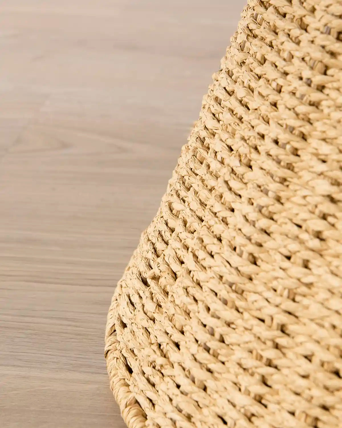 Close-up of the woven natural-fiber texture and tapered edge of the tree collar on a light wood floor.