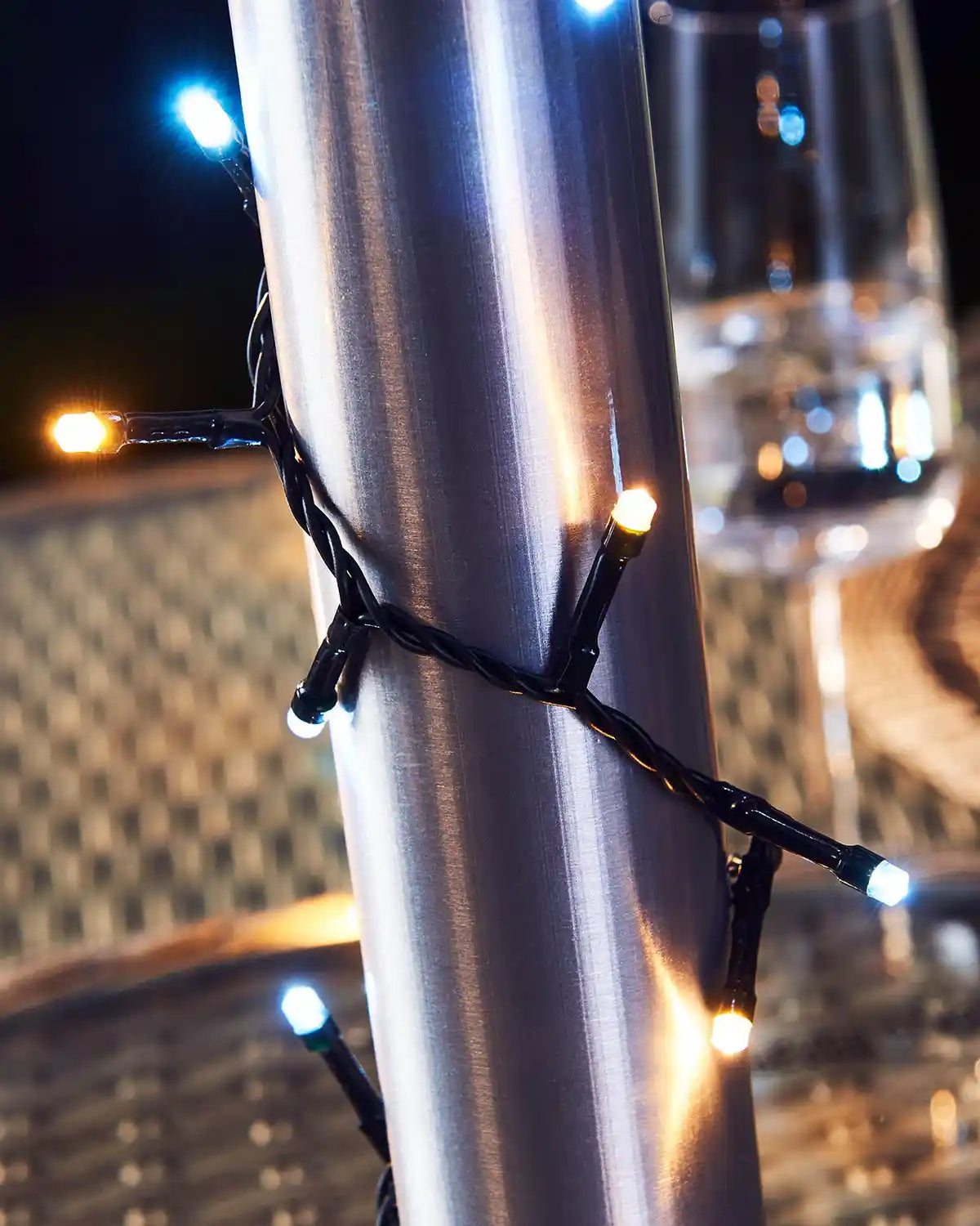 Close-up of umbrella pole with string lights wrapped around it against a blurred background