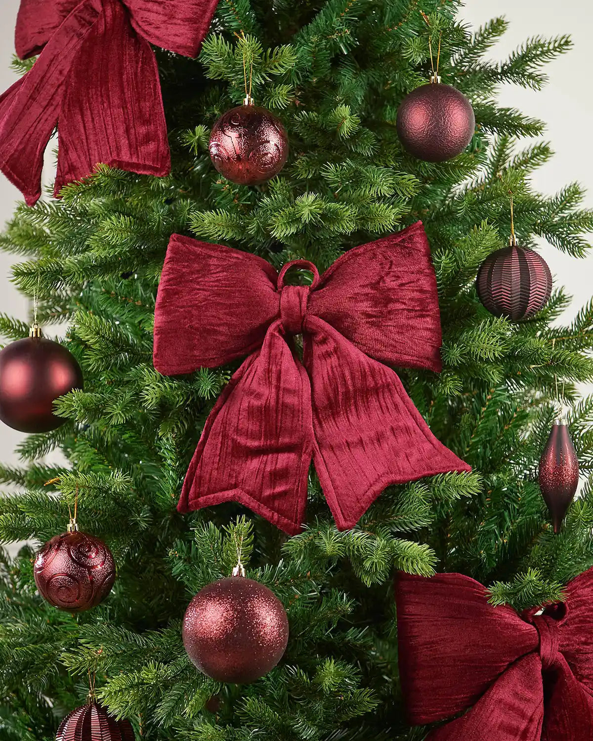 Vintage-style burgundy velvet bow hanging on a Christmas tree surrounded by burgundy baubles