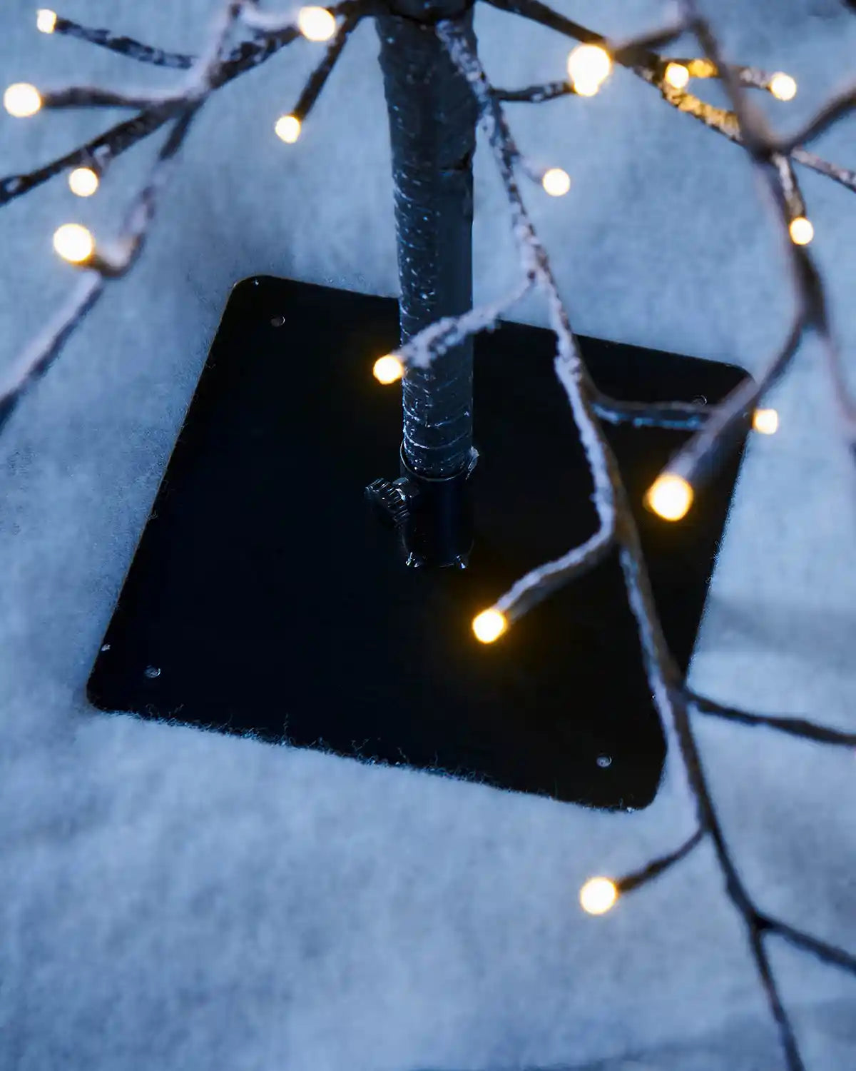 Close-up of warm white single lit bulbs and black tree base with snowy background