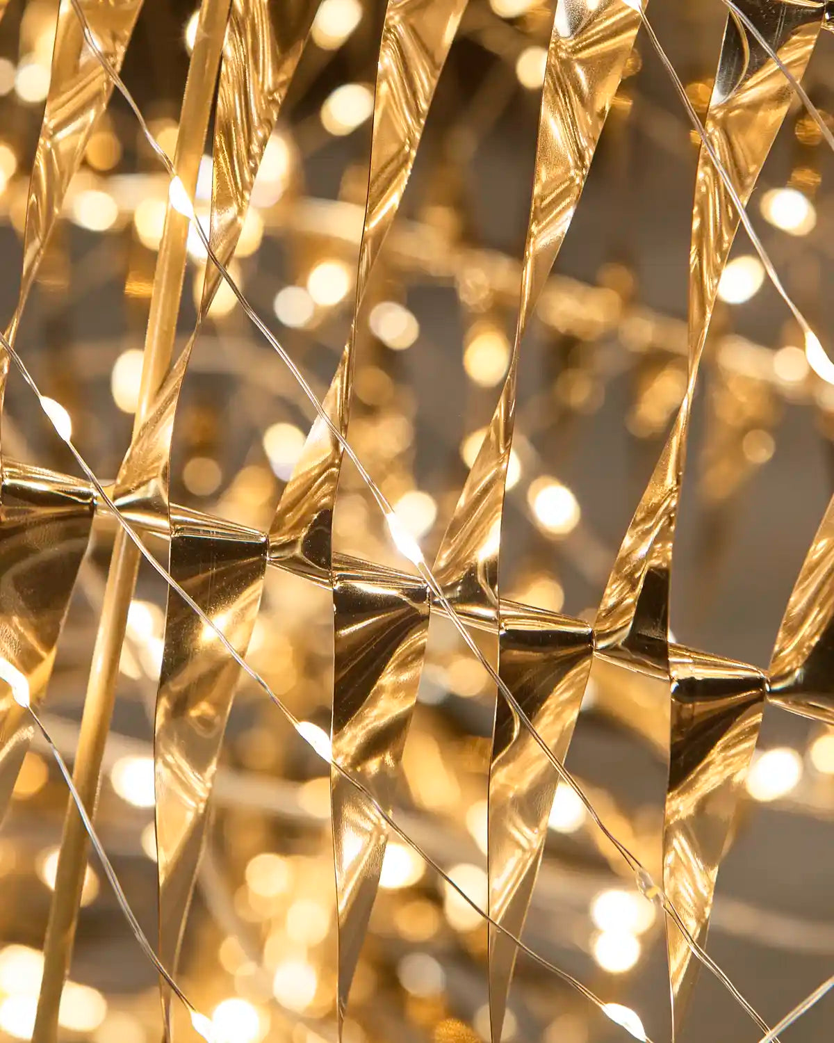 Close-up of warm white string lights reflecting off metallic gold triangular pennant flags, creating a sparkling bokeh effect.