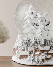 Close-up of snowman snow globe on dark wood surface in front of white wall