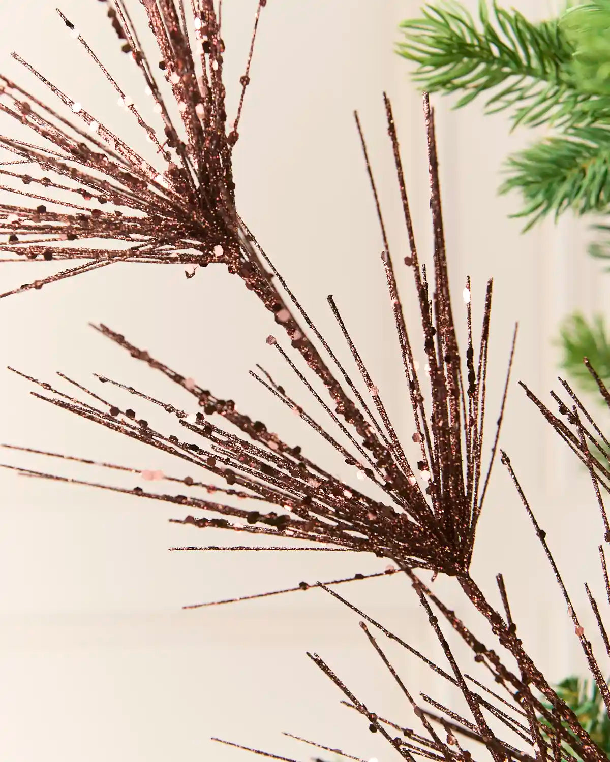 Close-up view of  Espresso  glitter firework branches extending from a central stem among the green branches of a Christmas tree
