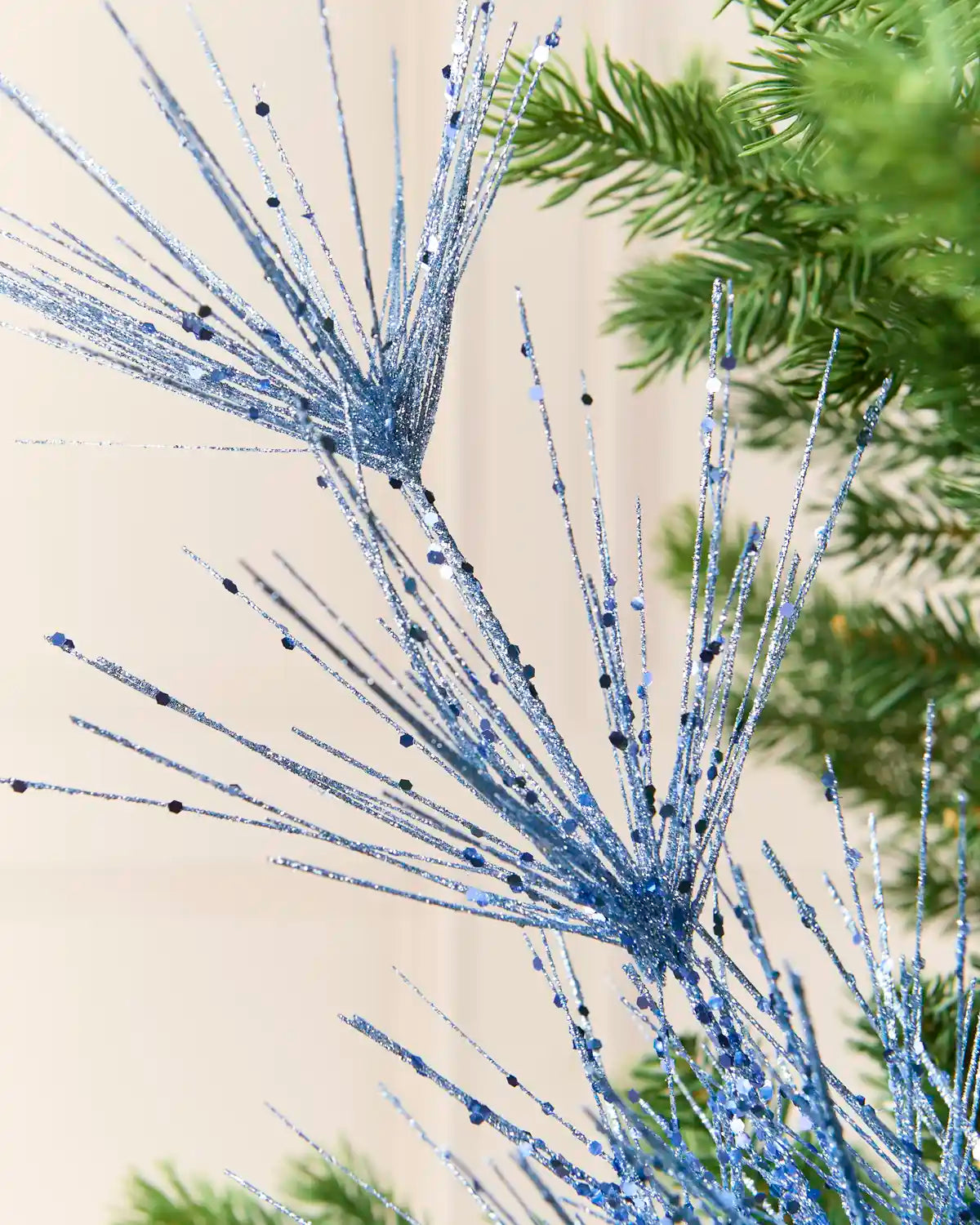 Close-up view of Ice Blue glitter firework branches extending from a central stem among the green branches of a Christmas tree
