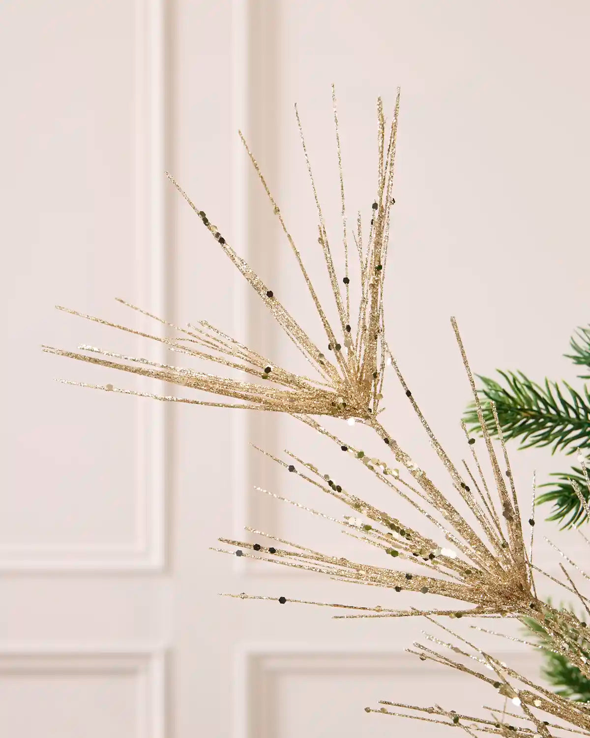 Close-up view of Latte glitter firework branches extending from a central stem among the green branches of a Christmas tree
