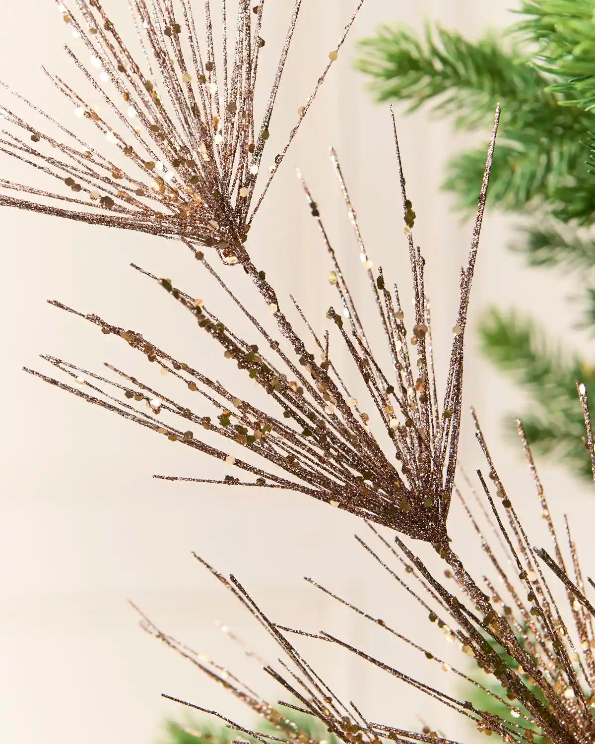 Close-up view of Mocha glitter firework branches extending from a central stem among the green branches of a Christmas tree
