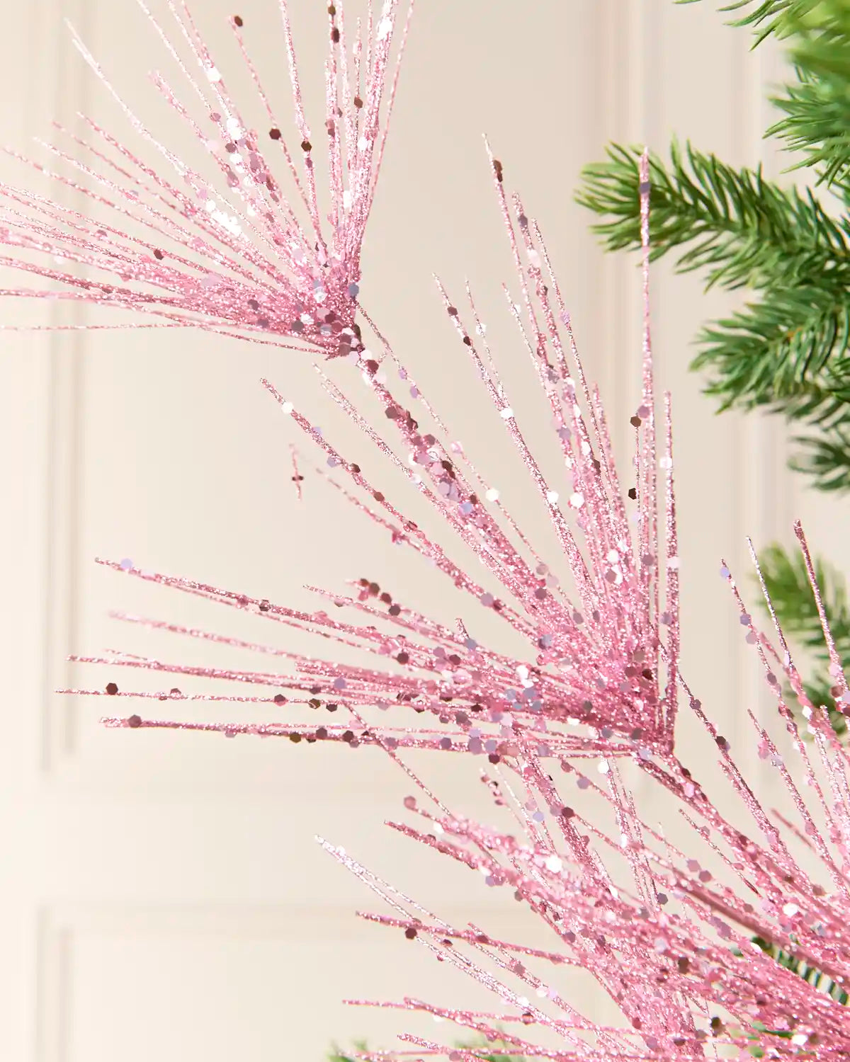 Close-up view of Pink glitter firework branches extending from a central stem among the green branches of a Christmas tree
