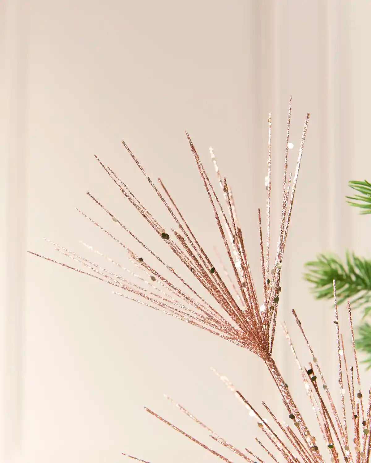 Close-up view of  Rose Gold  glitter firework branches extending from a central stem among the green branches of a Christmas tree
