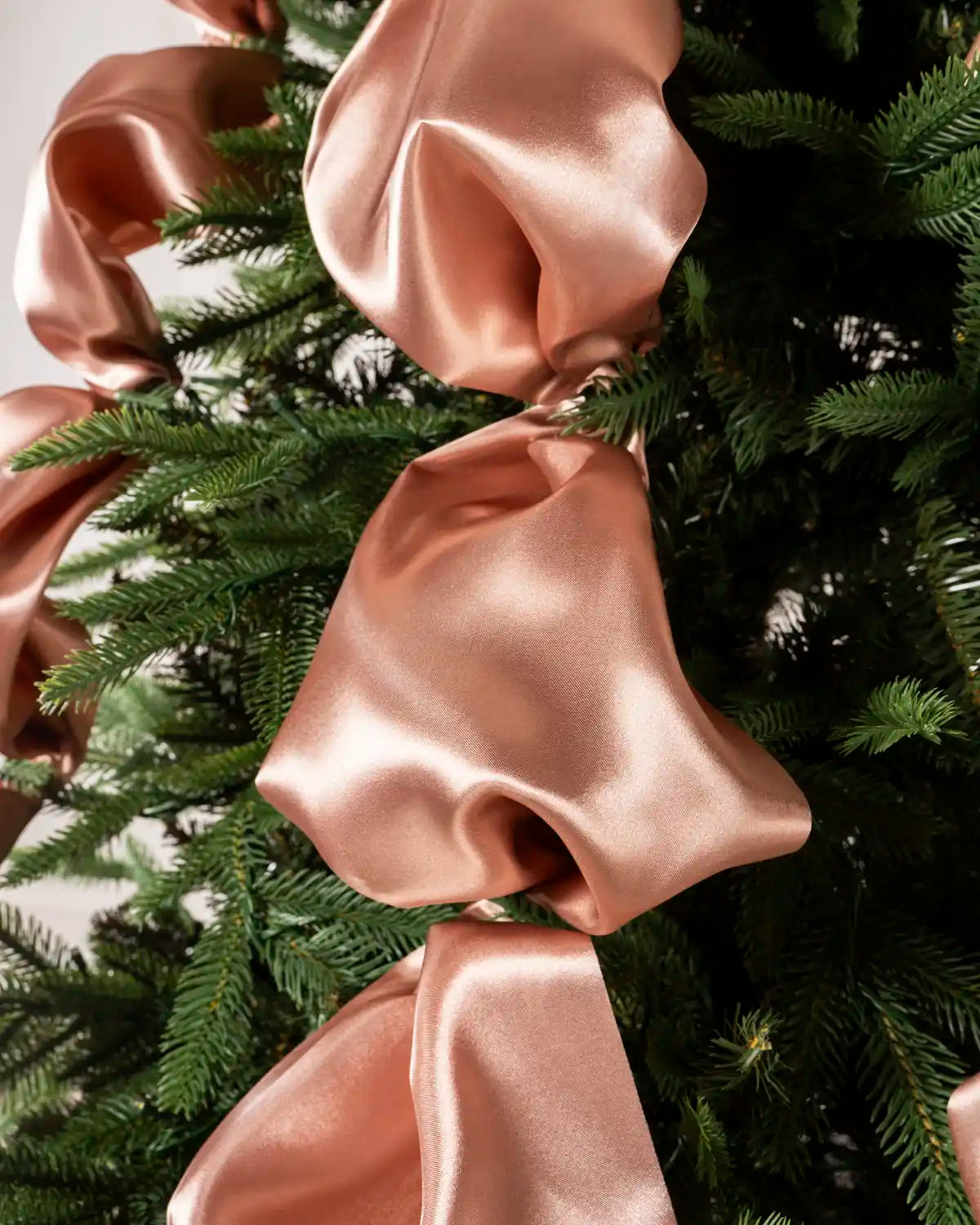 Close-up view of multiple rose gold satin ribbons arranged on green Christmas tree branches