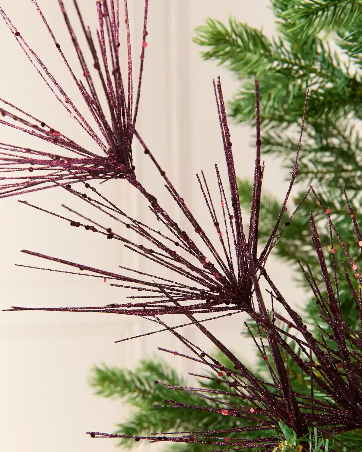 Close-up view of purple glitter firework branches extending from a central stem among the green branches of a Christmas tree