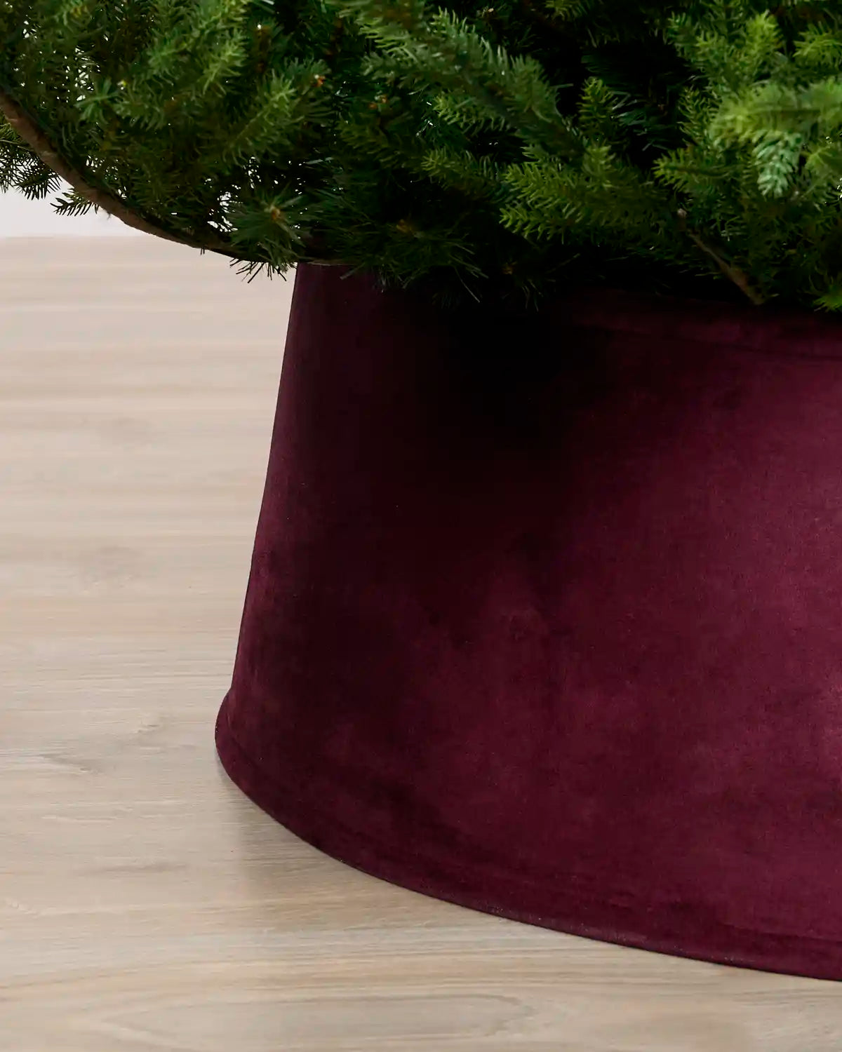 Close-up view of the burgundy velvet tree skirt, highlighting its rich texture and curved edge around the Christmas tree base